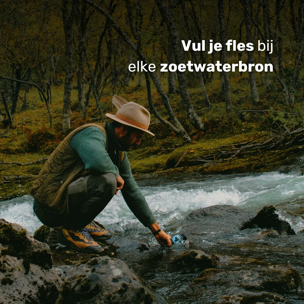 Man vult zijn BPA-vrije waterfles met een ingebouwd waterfilter direct uit een stromend riviertje tijdens een hike. Ideaal voor outdoor, survival, reizen en waterzuivering in de natuur.
